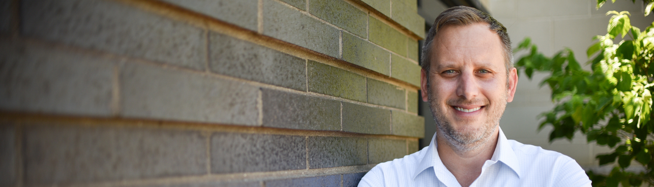 man smiling by brick wall outside